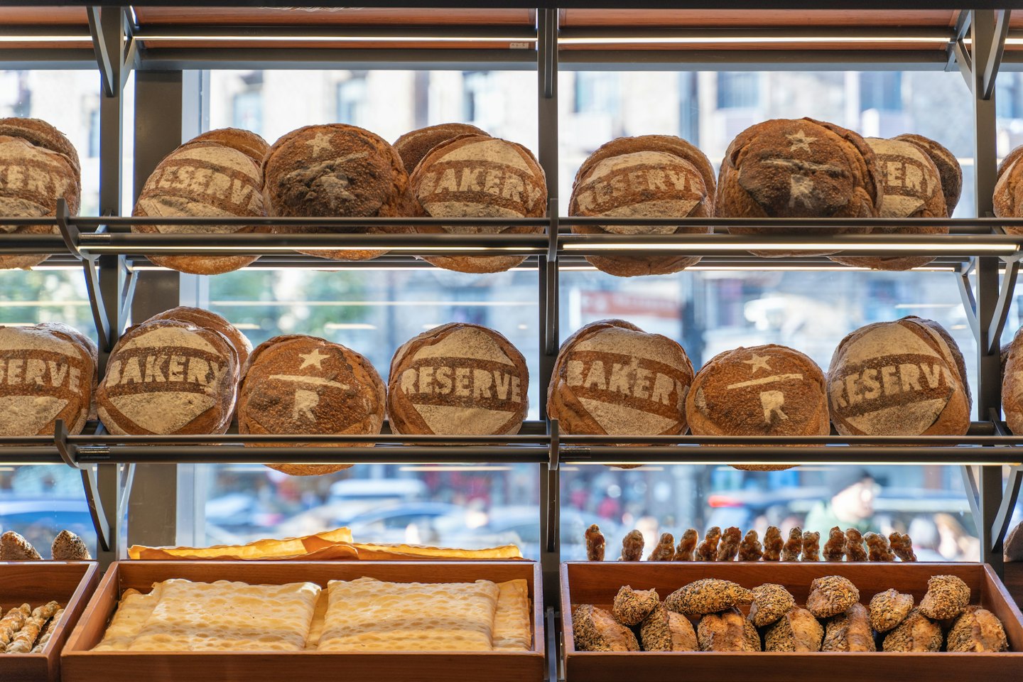 Artisan bread loaves displayed on bakery shelves behind a window.